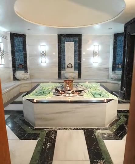 A hammam with a central marble platform, a copper bowl and tiled walls